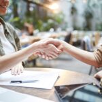 Women shaking hands across desk with paper work and pen