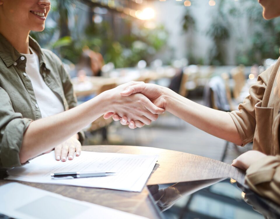 Women shaking hands across desk with paper work and pen