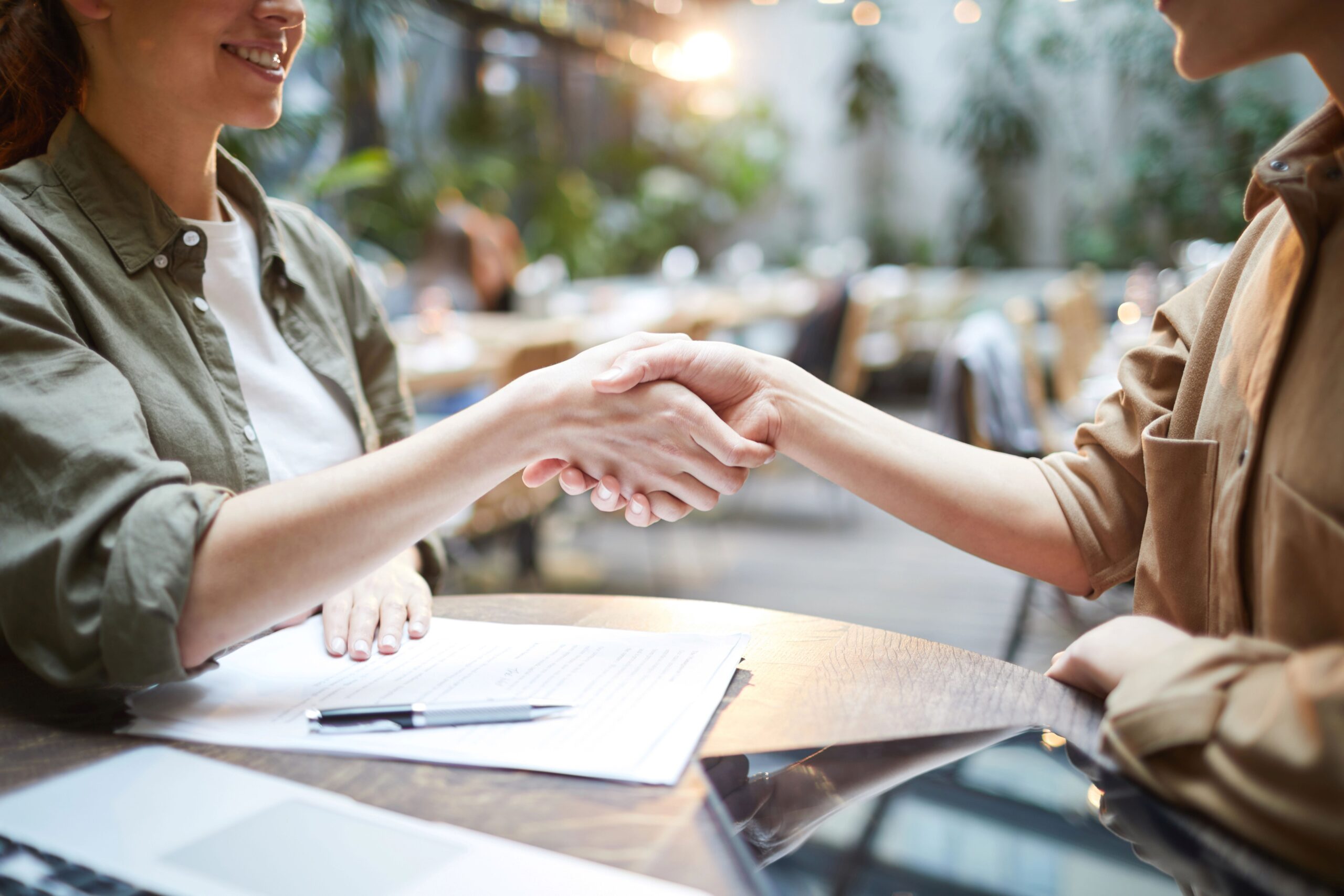 Women shaking hands across desk with paper work and pen