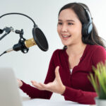 woman wearing headphones and speaking into a microphone recording a podcast episode