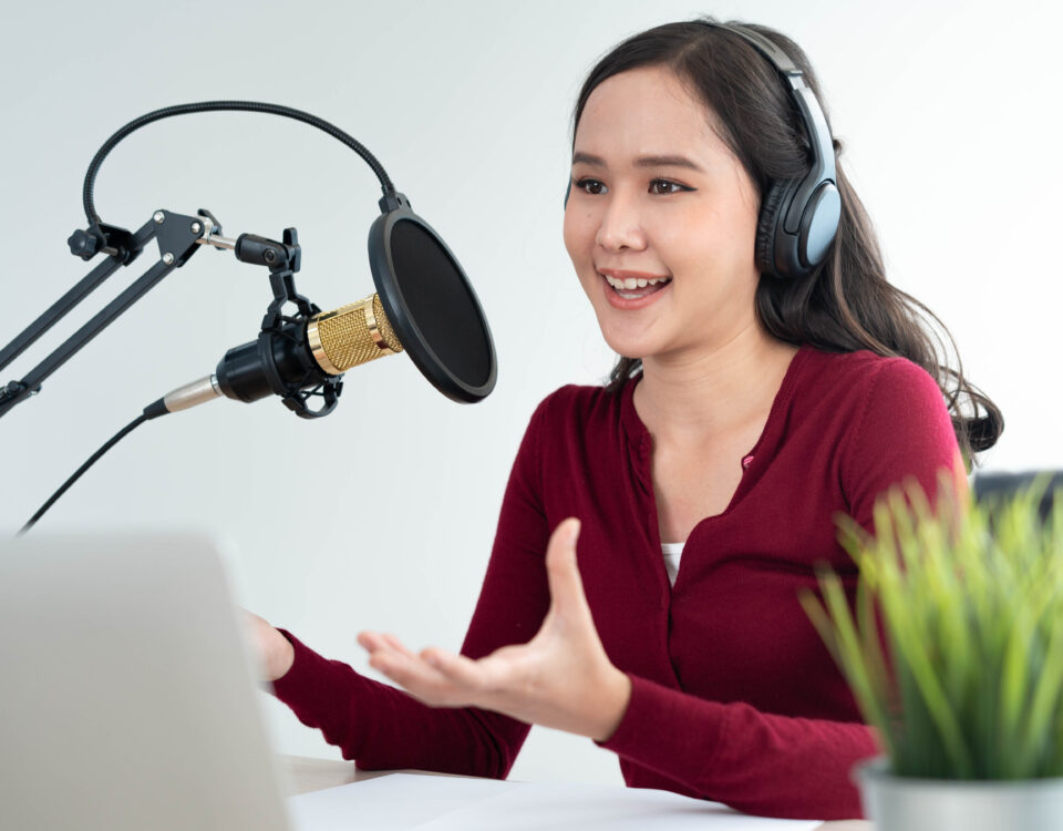 woman wearing headphones and speaking into a microphone recording a podcast episode